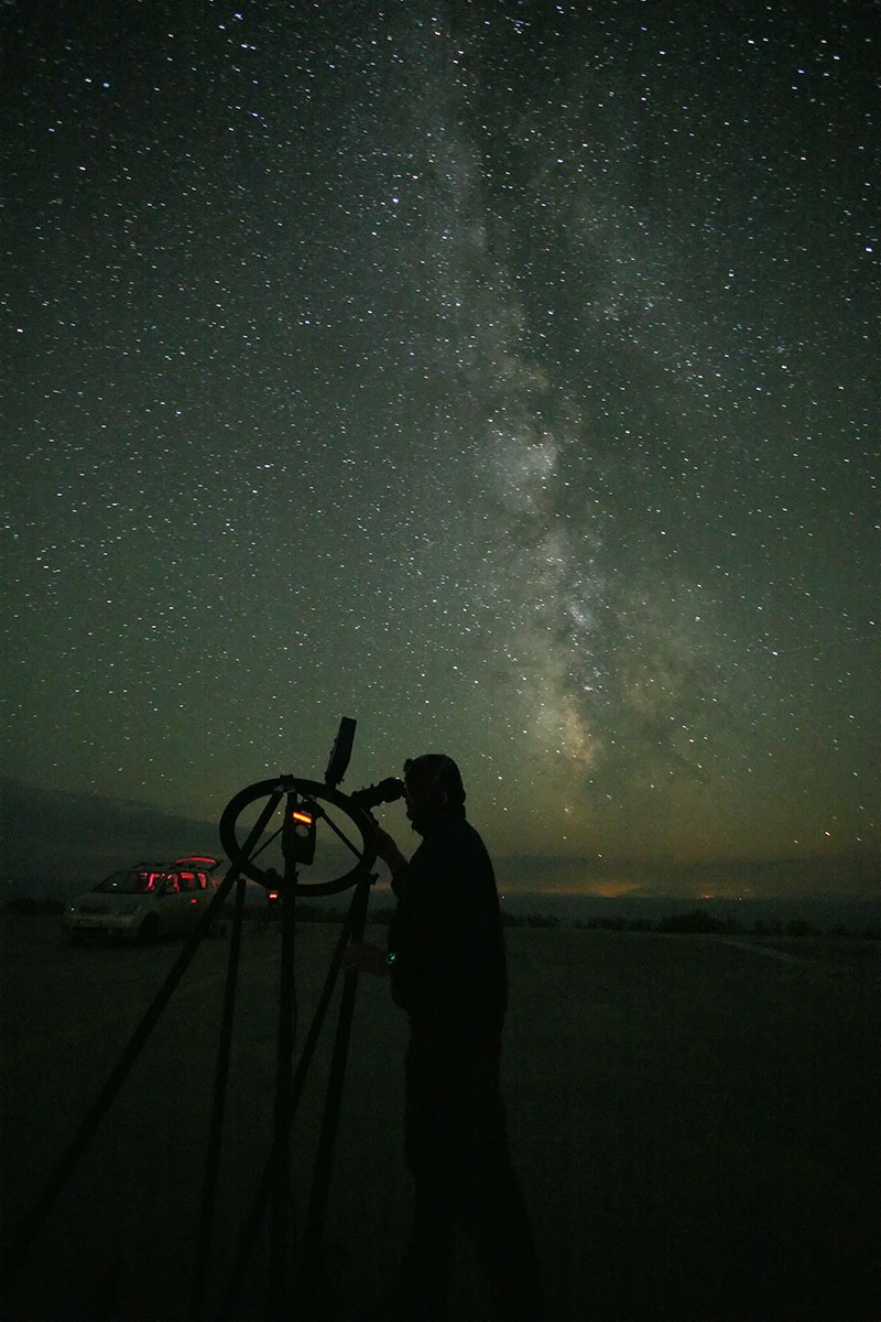 Ein nur als Silhouette erkennbarer Mann beobachtet in der Nacht mit einem Teleskop Sterne im Band der Milchstraße