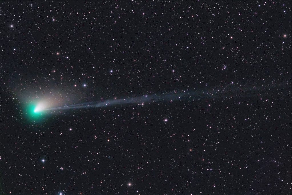 Ein Farbfoto zeigt die verschiedenen Komponenten des Kometen ZTF: Eine grünlich leuchtende Koma um den Kometenkern links, einen diffusen weiß-rötlichen Staubschweif, der nach oben rechts abströmt, und einen langen bläulichen Ionenschweif, der sich nach rechts bis über den Bildrand erstreckt.