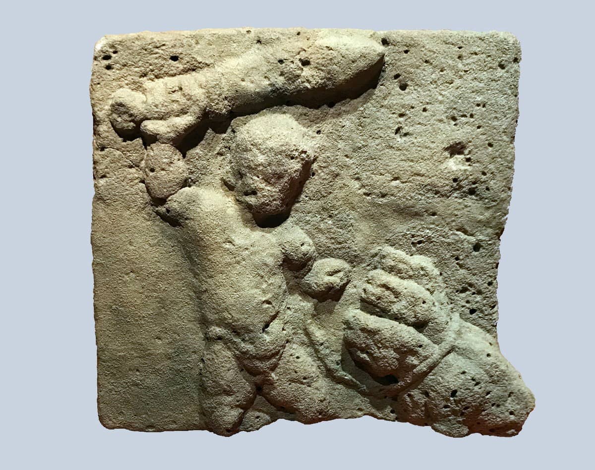 Das Fragment eines Steinreliefs zeigt Herkules, der in der rechten Hand ein Keule schwingt und mit der linken den dreiköpfigen Höllenhund Cerberus an einem Band aus der Unterwelt zerrt.
